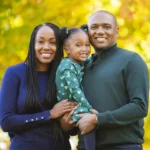 portrait of an african american father, mother and toddler daughter smiling in a park