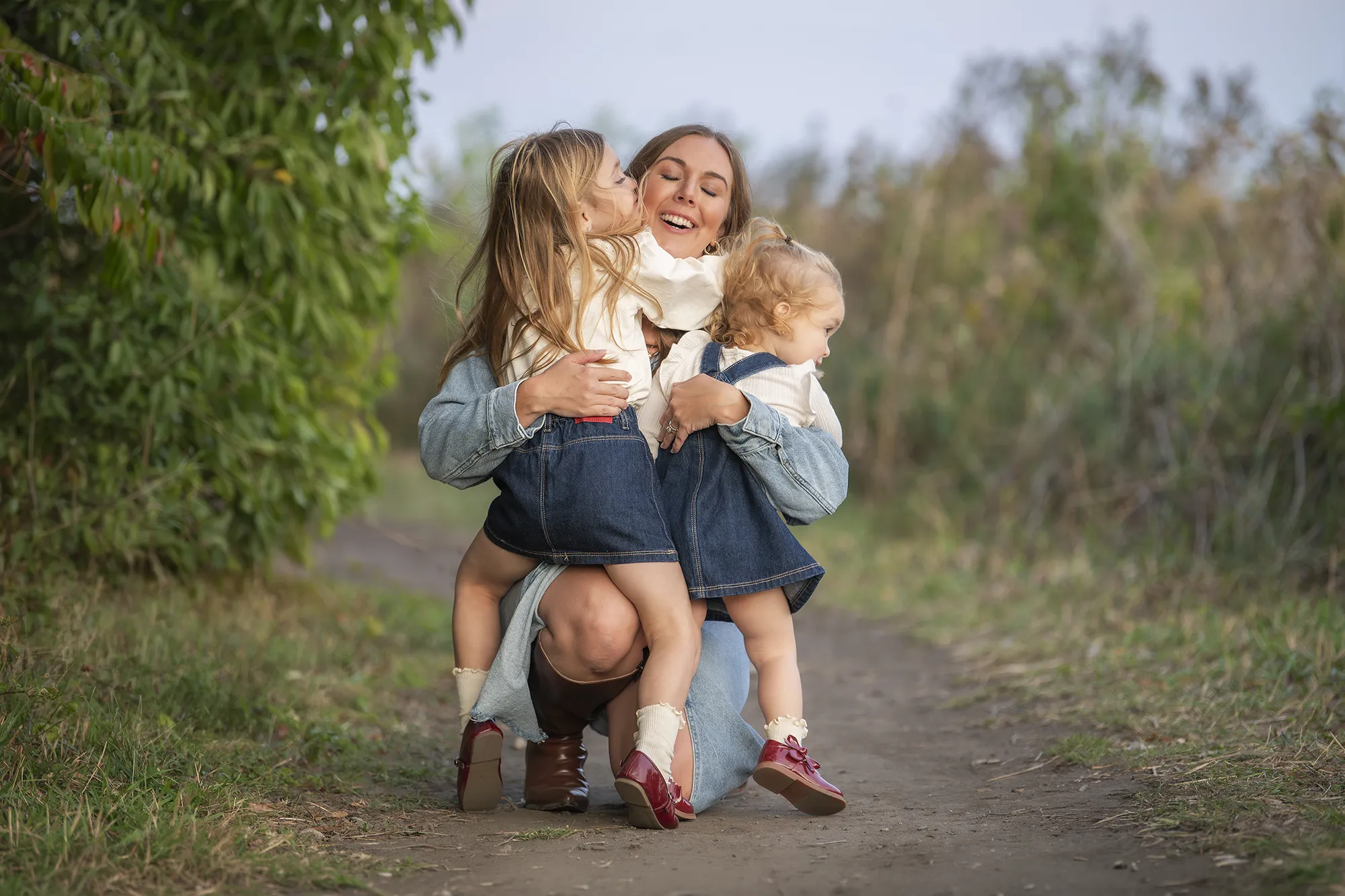 two toddler caucasian girls hugging and kissing their mother at a park in Glencoe