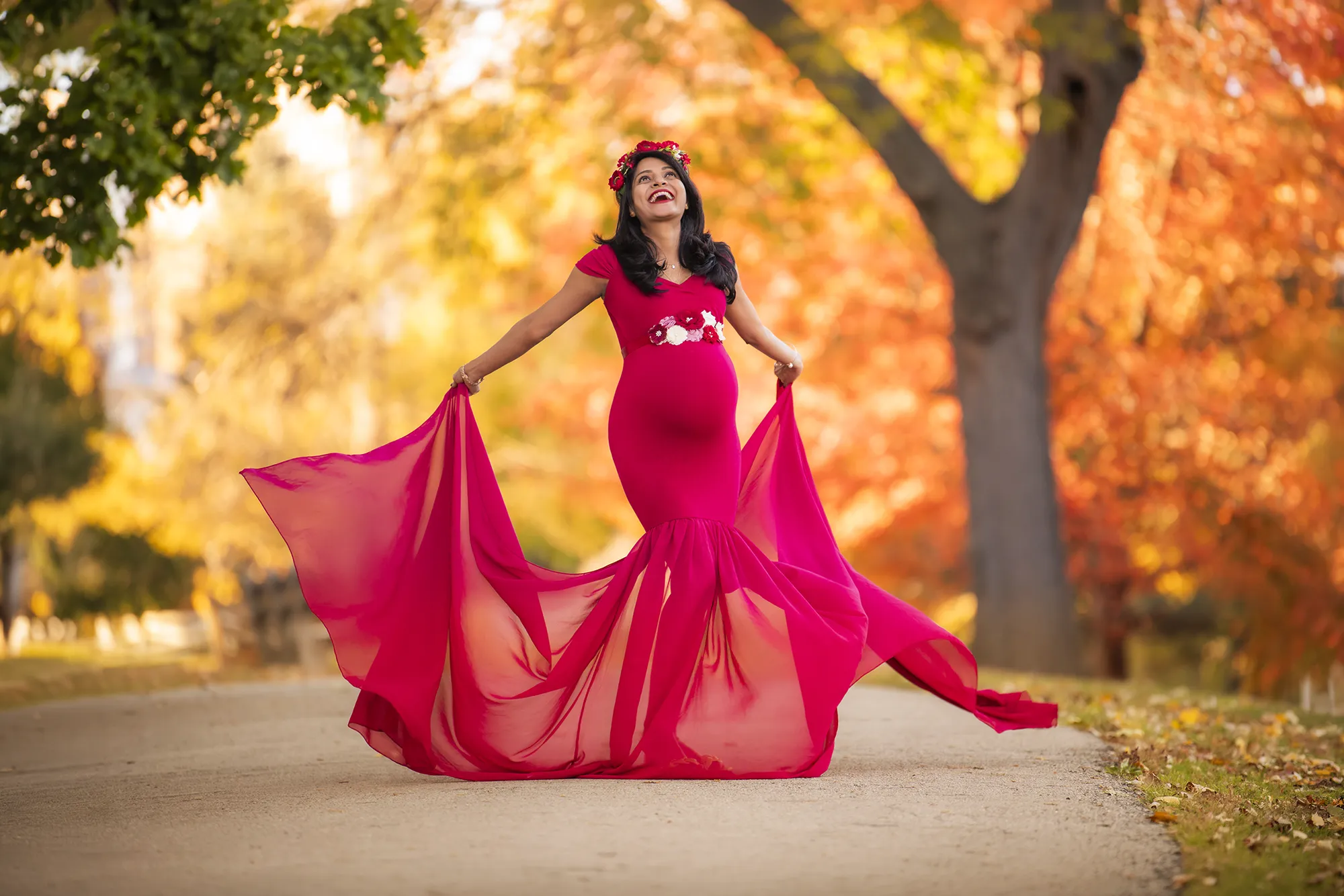 Indian expecting mother wearing a beautiful red gown dancing an laughing at a park in Winnetka